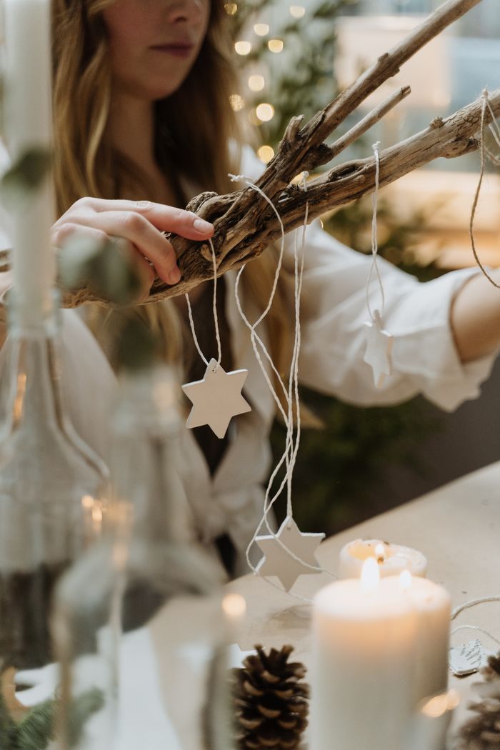 A woman arranges handmade star decorations on a branch in a cozy indoor setting.